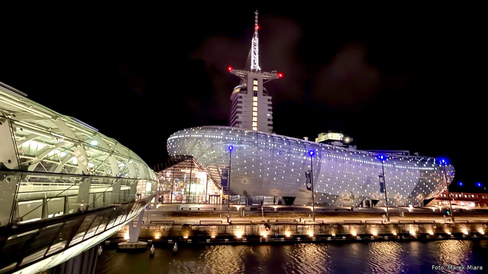 Das Klimahaus Bremerhaven bei Nacht, beleuchtet am Hafenbecken, dahinter das Atlantic Hotel Sail City
