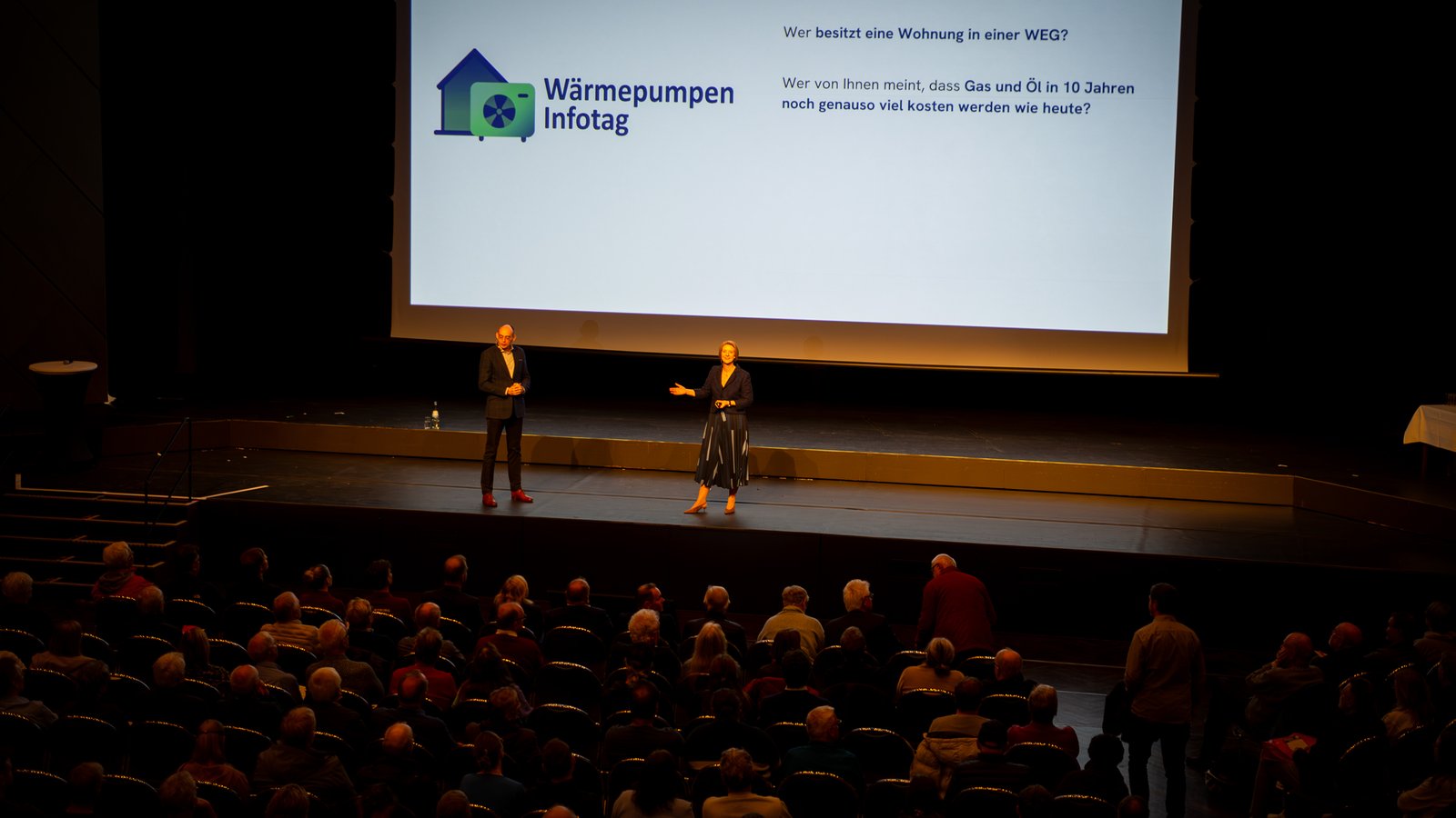 Anja Floetenmeyer-Woltmann und Dr. Marek Miara auf der Bühne, Logo Wärmepumpen-Infotag, Frage an den Saal