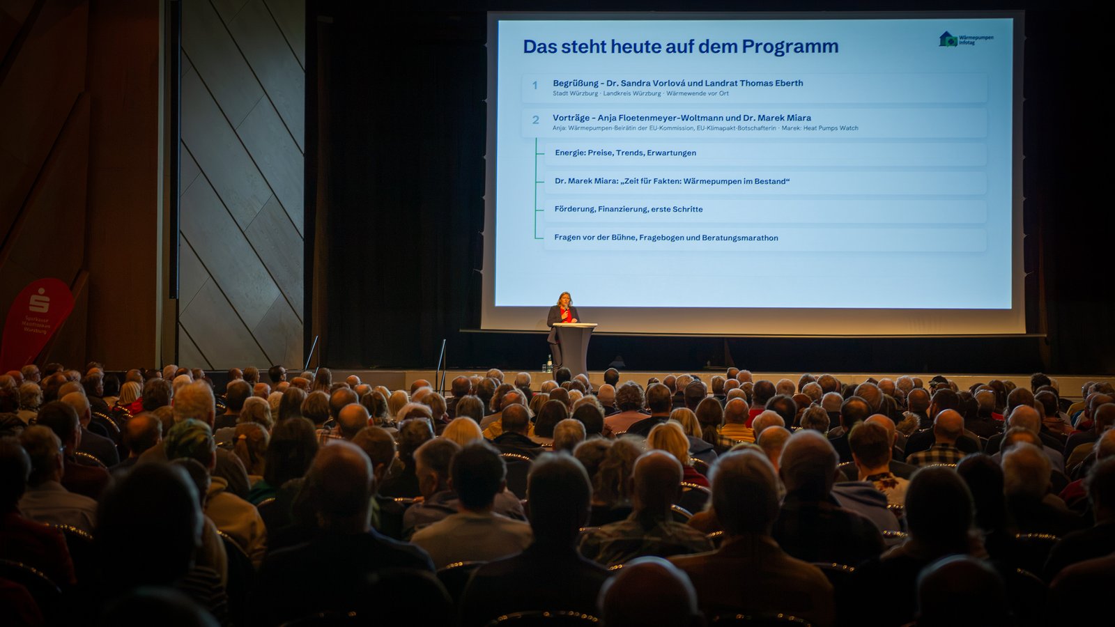 Begrüßung am Rednerpult vor dem vollen Saal